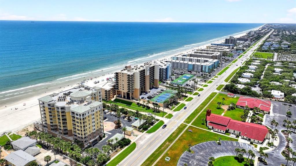 An aerial view shows beachfront high-rise condominiums, a road, and a church with red roofs — 4139 S ATLANTIC AVENUE UNIT B409, NEW SMYRNA BEACH, FL