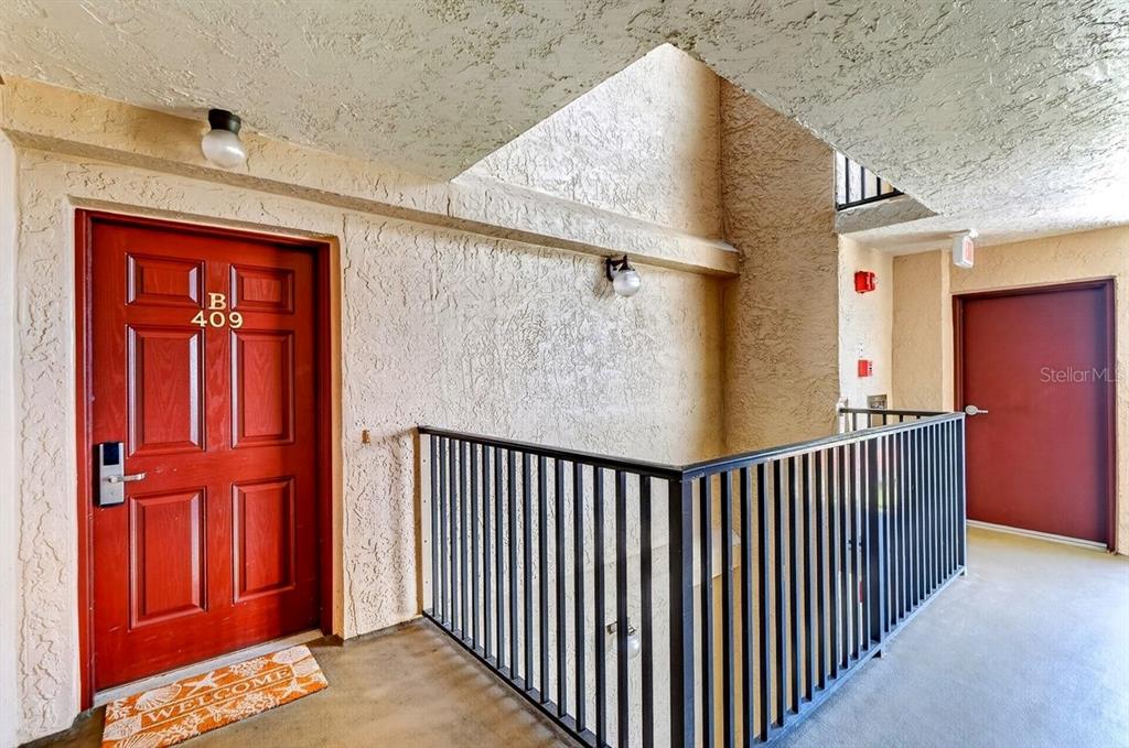 An exterior hallway features a red door labeled B 409, a black railing, and stucco walls — 4139 S ATLANTIC AVENUE UNIT B409, NEW SMYRNA BEACH, FL