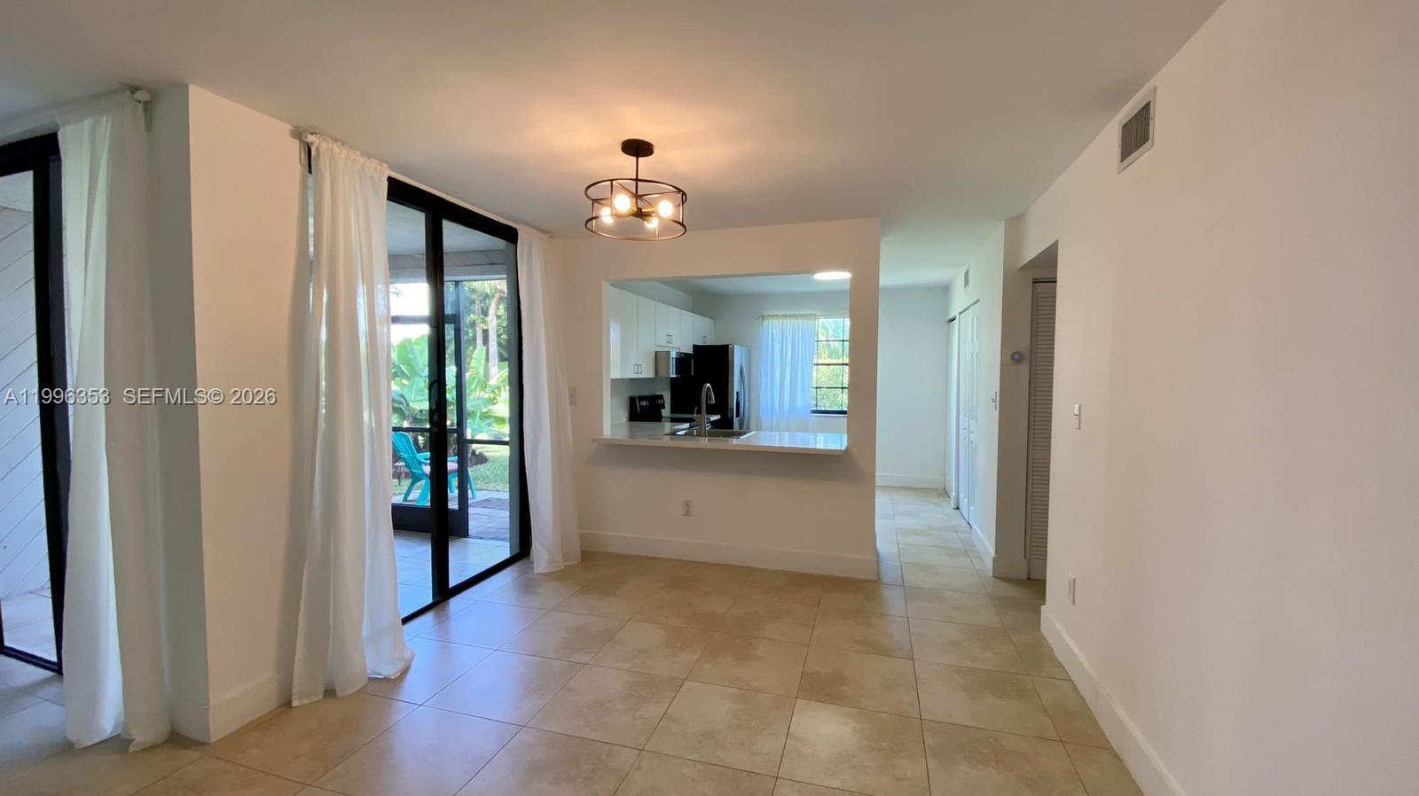 A dining area with tile floors leads to a kitchen pass-through and sliding glass doors — 3552 Magellan Cir # 126, Aventura FL 33180, AVENTURA, FL