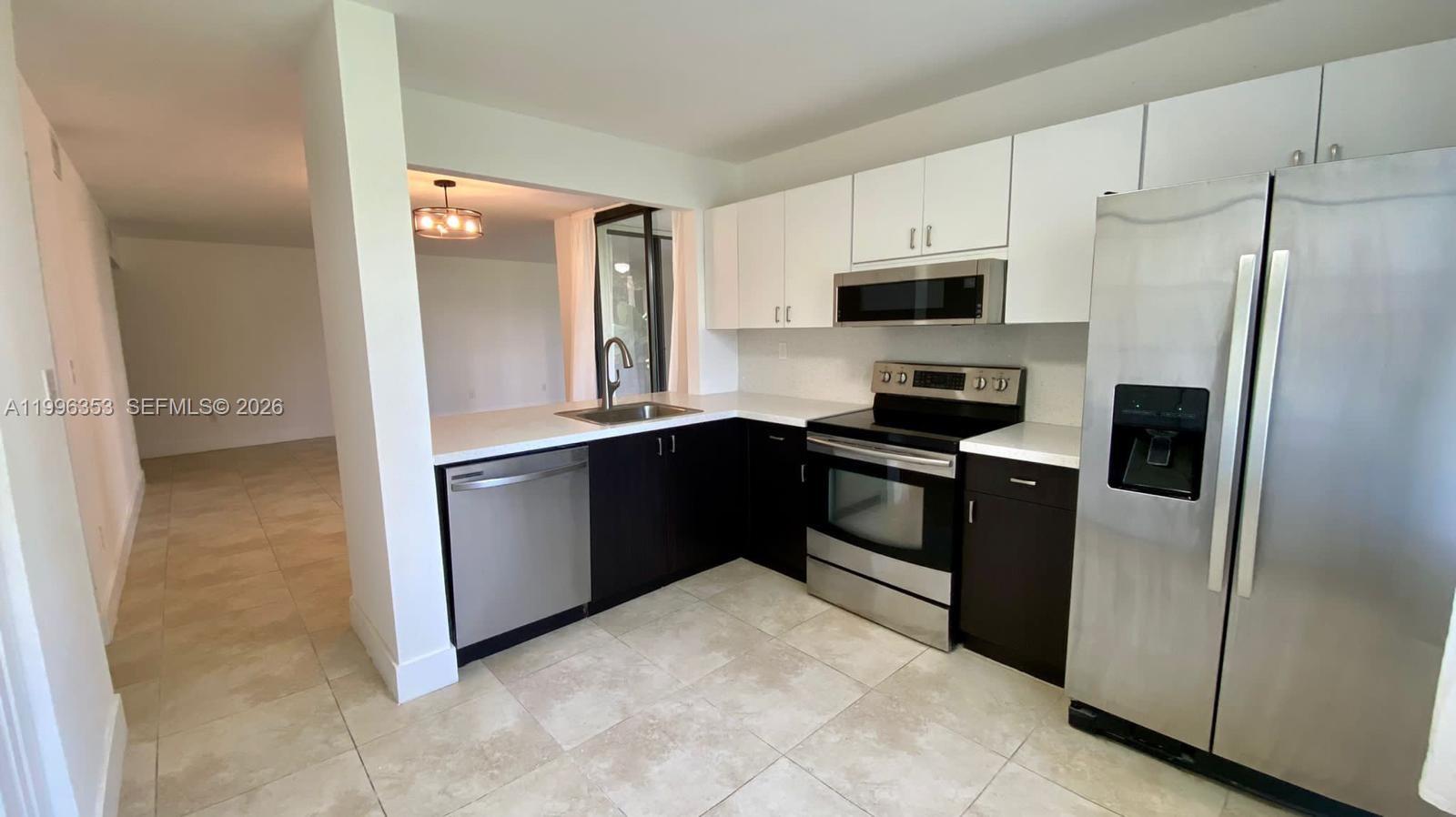 A kitchen features dark lower cabinets, white upper cabinets, stainless steel appliances, and tile flooring — 3552 Magellan Cir # 126, Aventura FL 33180, AVENTURA, FL