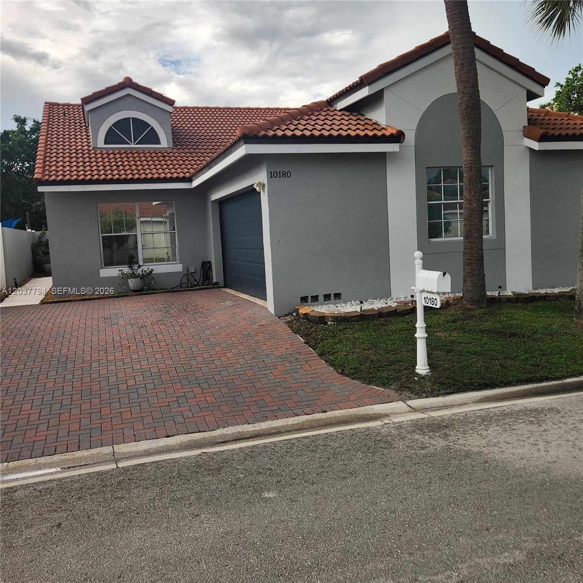 A gray single-story house features a red tile roof, brick driveway, and a white mailbox — 10180 Fanfare Dr # 10180, Boca Raton FL 33428, BOCA RATON, FL