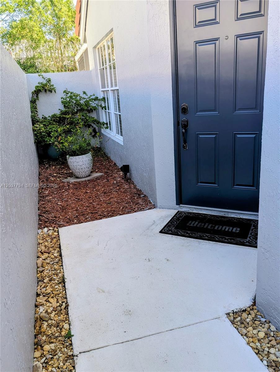 A dark blue front door opens onto a concrete entryway with a small garden bed — 10180 Fanfare Dr # 10180, Boca Raton FL 33428, BOCA RATON, FL