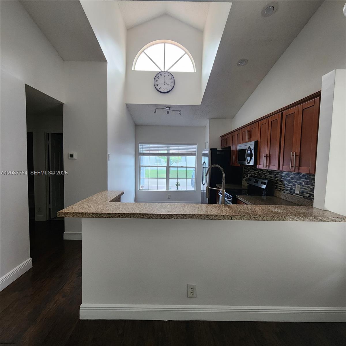 A kitchen features a granite breakfast bar, wood cabinets, and a high ceiling with a clock — 10180 Fanfare Dr # 10180, Boca Raton FL 33428, BOCA RATON, FL