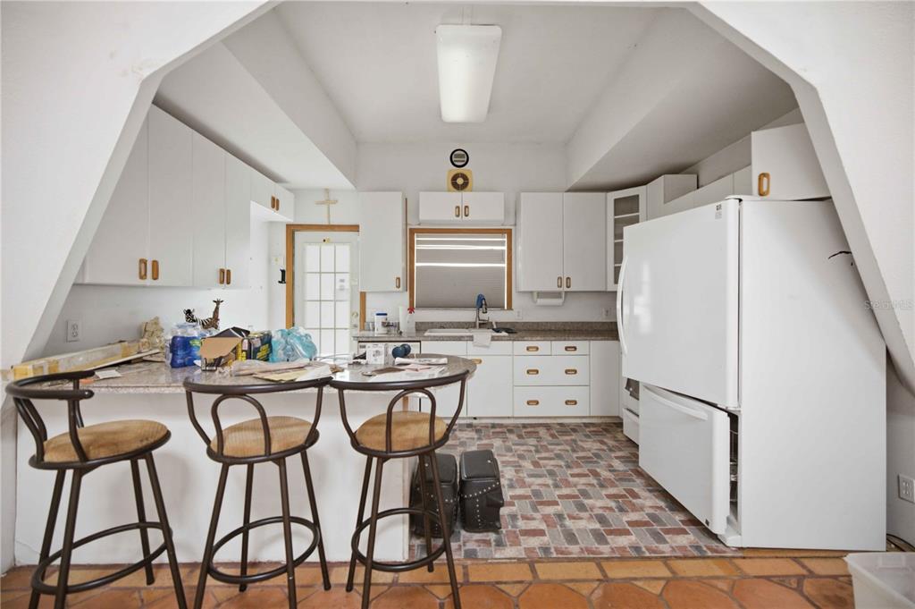 A kitchen features white cabinetry, a brick-patterned floor, a breakfast bar, and a white refrigerator — 12897 NW HIGHWAY 225, REDDICK, FL
