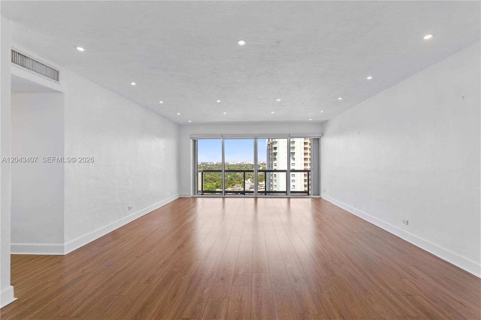 A spacious, empty room features white walls, recessed lighting, and light brown wood flooring — 2451 Brickell Ave, Miami FL 33129, MIAMI, FL