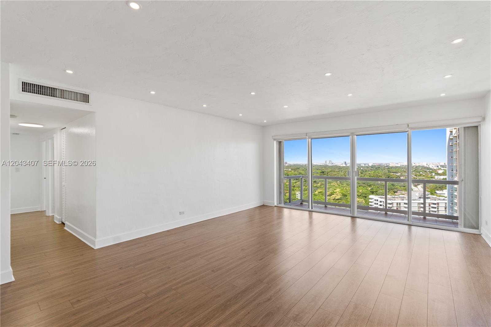 An empty living room features light wood-look flooring, white walls, recessed lighting, and balcony access — 2451 Brickell Ave, Miami FL 33129, MIAMI, FL