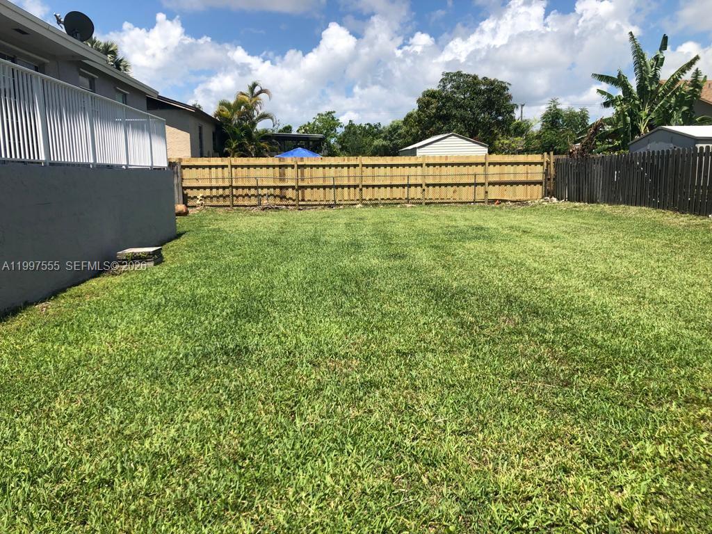 A grassy backyard features a wooden fence, a concrete wall, and a raised deck — 9771 SW 211th st, Cutler Bay FL 33189, CUTLER BAY, FL