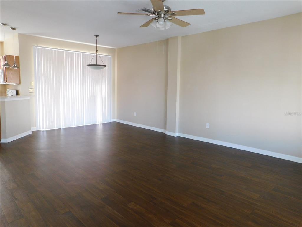 A spacious living room features dark wood-look flooring, beige walls, and a ceiling fan — 12450 COUNTRY WHITE CIRCLE, TAMPA, FL