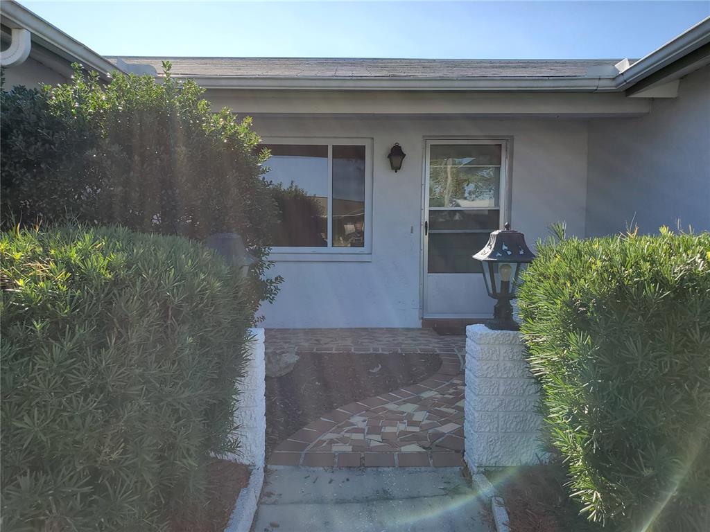 A front entrance features a tiled walkway, a storm door, and two large green bushes — 7304 LINCOLN PARK LANE, PORT RICHEY, FL