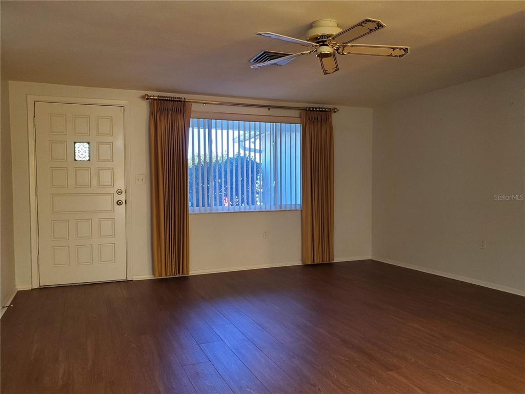 A living room features wood-look flooring, a ceiling fan, and a white front door — 7304 LINCOLN PARK LANE, PORT RICHEY, FL
