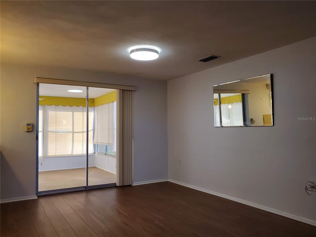 A living room with wood-look flooring, a sliding glass door, and a wall-mounted mirror — 7304 LINCOLN PARK LANE, PORT RICHEY, FL