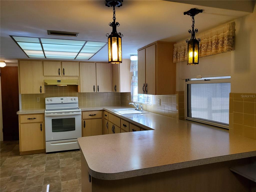 A kitchen features light wood cabinets, tan laminate countertops, a white stove, and pendant lighting — 7304 LINCOLN PARK LANE, PORT RICHEY, FL
