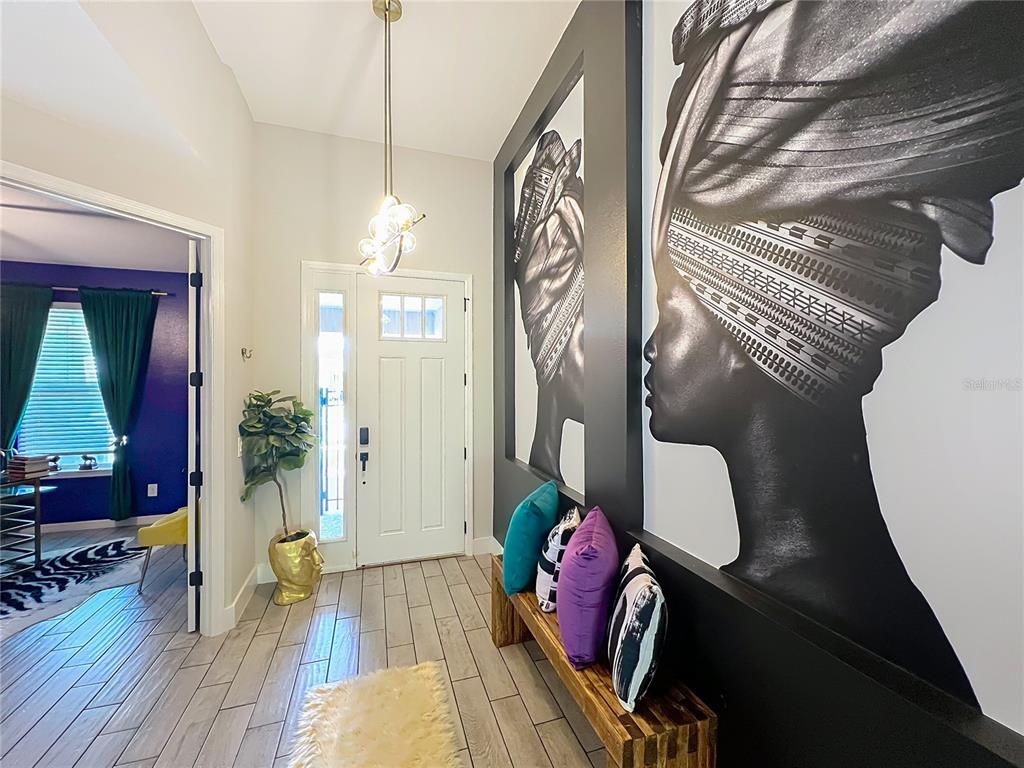 An entryway features wood-look tile flooring, a wooden bench with colorful pillows, and large wall art — 991 LAKESIDE ESTATES DRIVE, APOPKA, FL