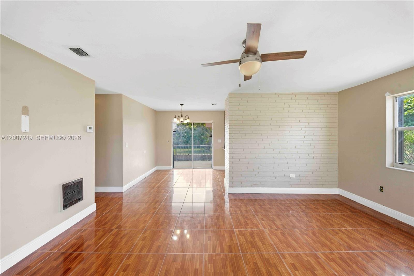 An empty living room features tan walls, a brick accent wall, and tiled flooring — 2724 Acapulco Dr, Miramar FL 33023, MIRAMAR, FL