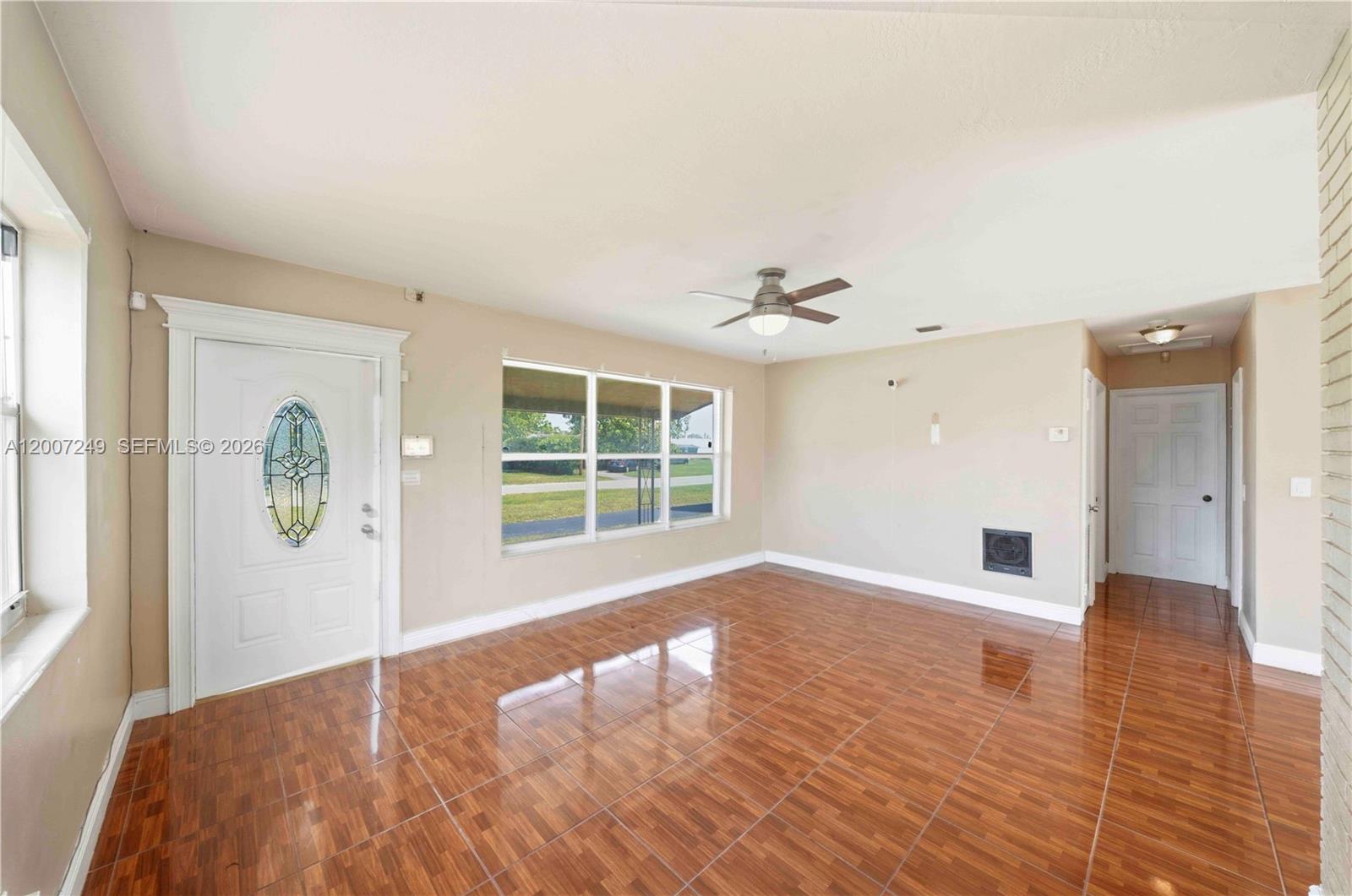 An empty living room features glossy wood-look tile flooring, a ceiling fan, and a front door — 2724 Acapulco Dr, Miramar FL 33023, MIRAMAR, FL