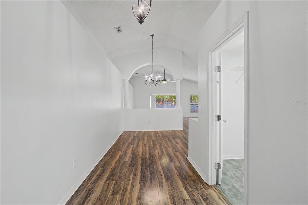 An empty room with wood-look flooring, white walls, vaulted ceilings, and two hanging light fixtures — 605 SWAN RANGE ROAD, ORANGE CITY, FL