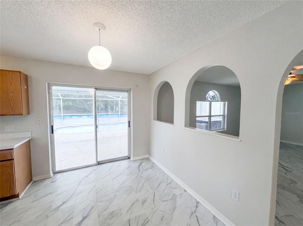 A dining area features white marble-look tile flooring, arched wall cutouts, and sliding glass patio doors — 5191 QUINTILIS STREET, SPRING HILL, FL