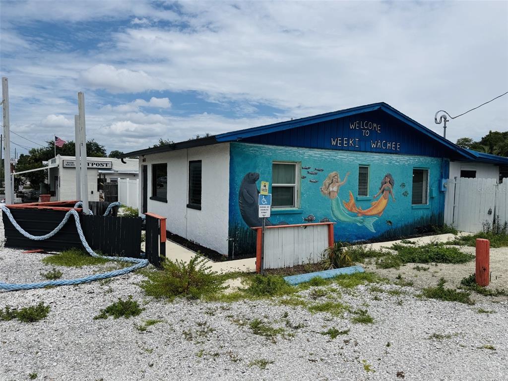 A white building with a blue roof features a mural of mermaids and a manatee — 8061 CORTEZ BOULEVARD, WEEKI WACHEE, FL