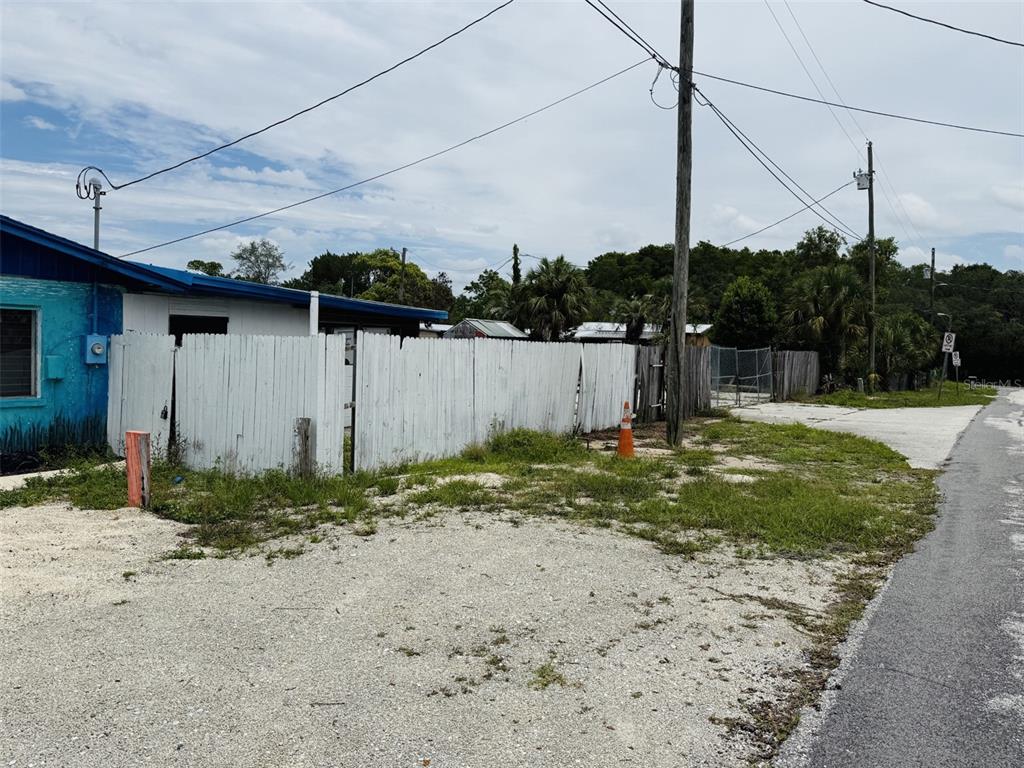 A white wooden fence encloses a property next to a gravel area and paved road — 8061 CORTEZ BOULEVARD, WEEKI WACHEE, FL