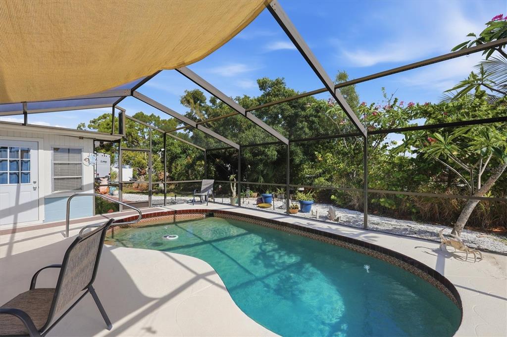 A screened-in patio features a kidney-shaped swimming pool and a tan shade sail overhead — 852 E 6TH STREET, ENGLEWOOD, FL