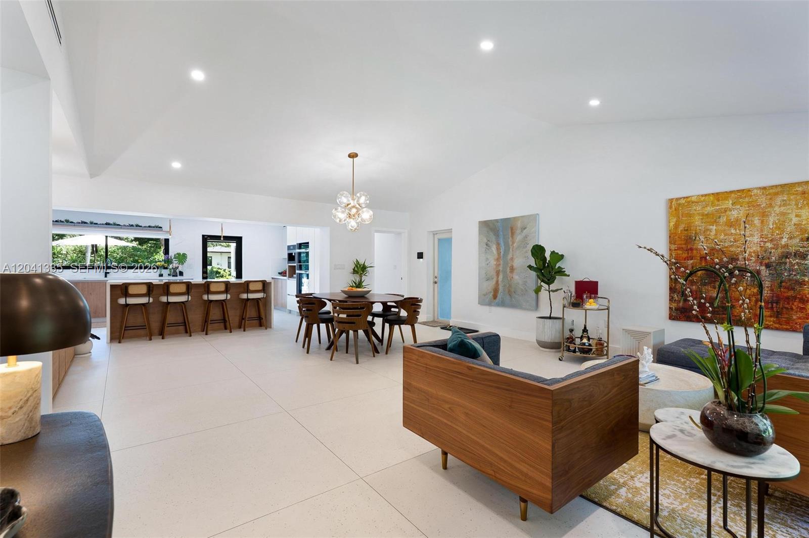 An open-concept living and dining area features white tile floors, vaulted ceilings, and modern furniture — 360 NE 91st St, Miami Shores FL 33138, MIAMI SHORES, FL