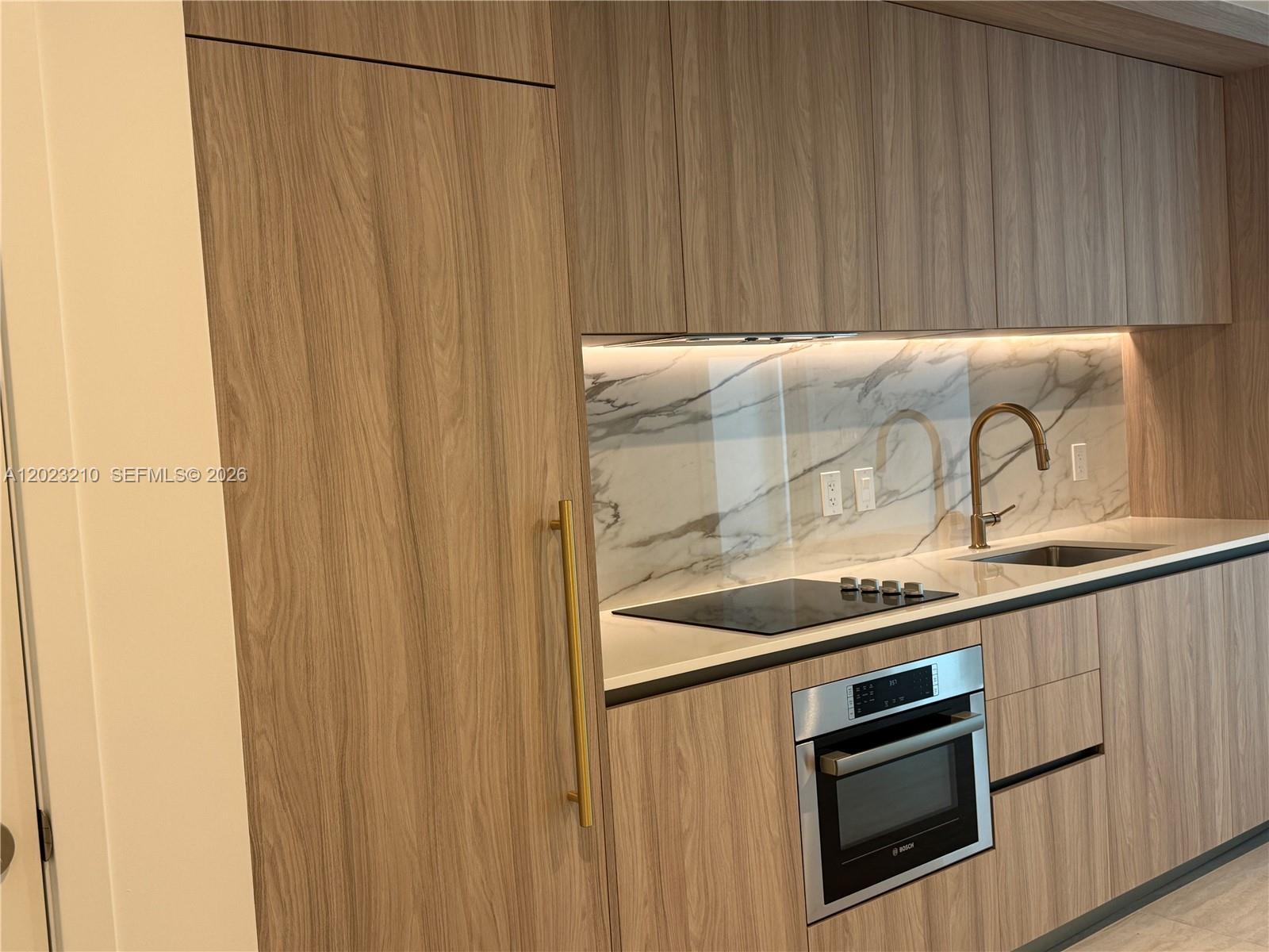 A modern kitchen features wood-grain cabinets, a marble backsplash, and stainless steel appliances — 77 SE 5th ST # 2111, Miami FL 33131, MIAMI, FL