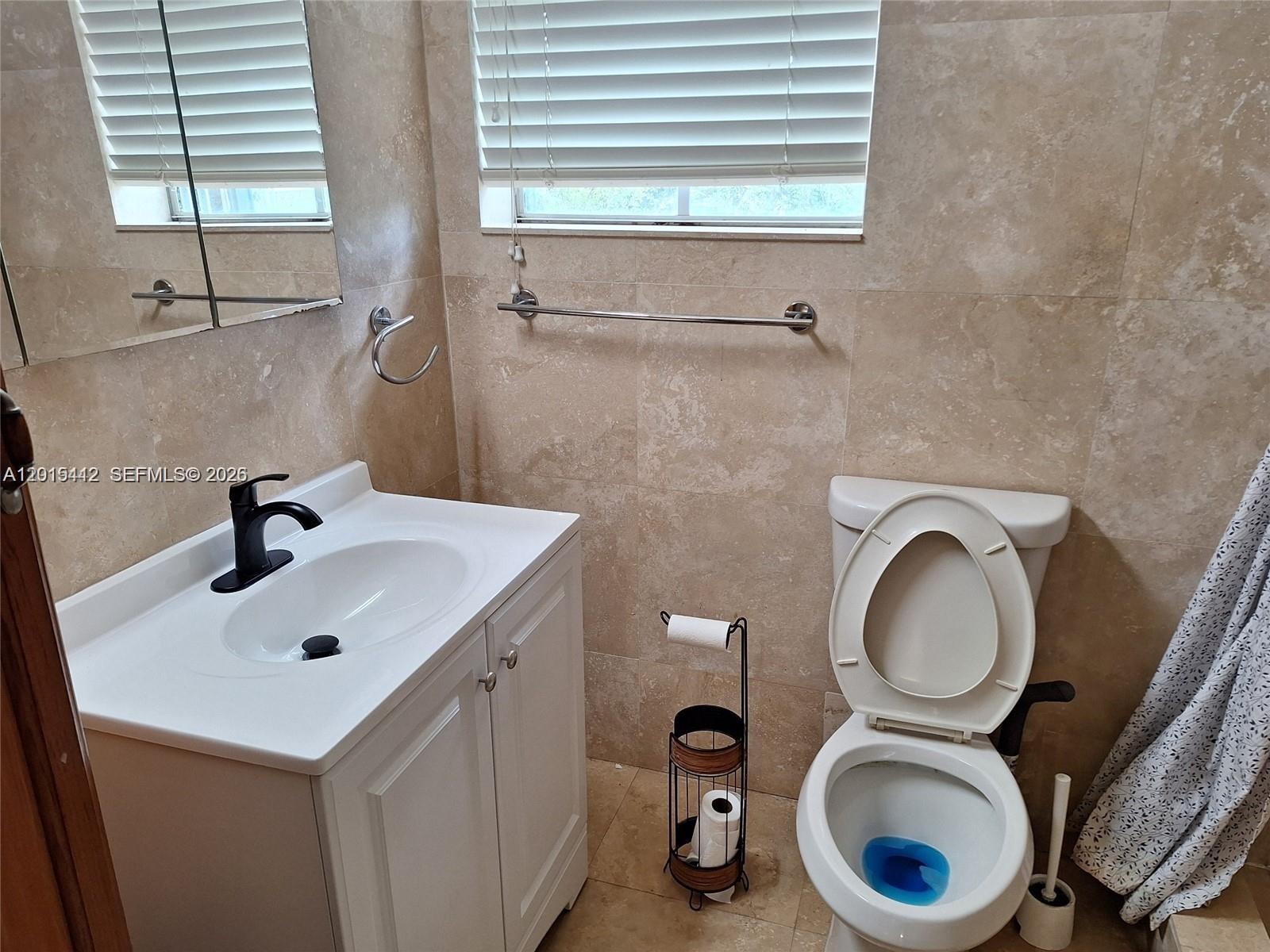 A bathroom features a white vanity, a toilet, and beige tiled walls — 2199 NE 182nd St # 0, North Miami Beach FL 33162, NORTH MIAMI BEACH, FL