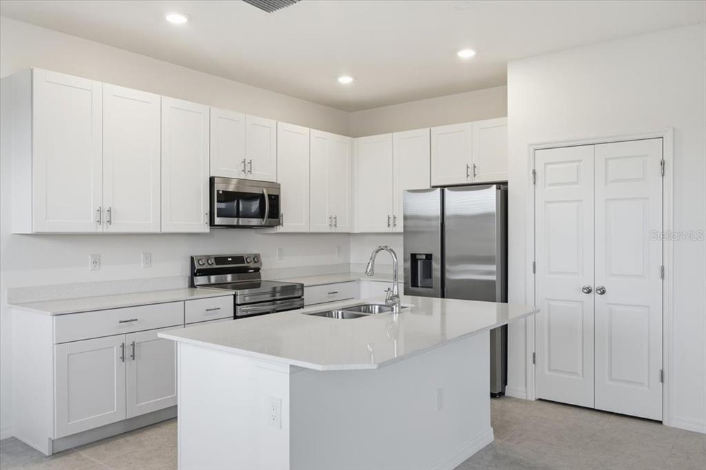 A modern kitchen features white cabinetry, stainless steel appliances, and a central island with countertops — 167 BOTTLE BRUSH DRIVE, HAINES CITY, FL