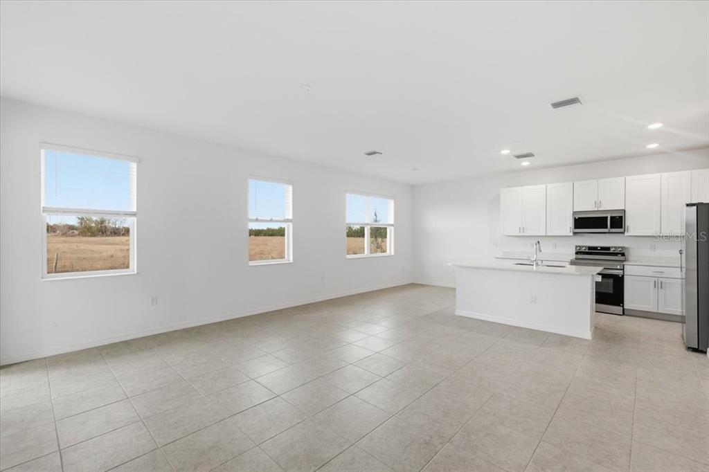 An open-concept kitchen and living area with white cabinets, stainless appliances, and tile flooring — 167 BOTTLE BRUSH DRIVE, HAINES CITY, FL