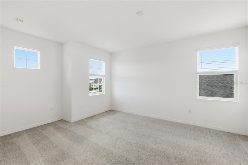 An empty bedroom features white walls, gray carpet, and three windows — 167 BOTTLE BRUSH DRIVE, HAINES CITY, FL