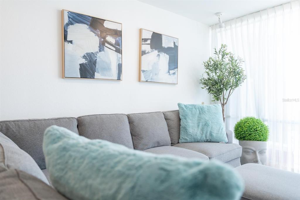 A gray sectional sofa sits in a living room with abstract wall art and plants — 6165 AV, ISLA VERDE UNIT 669, CAROLINA, PR