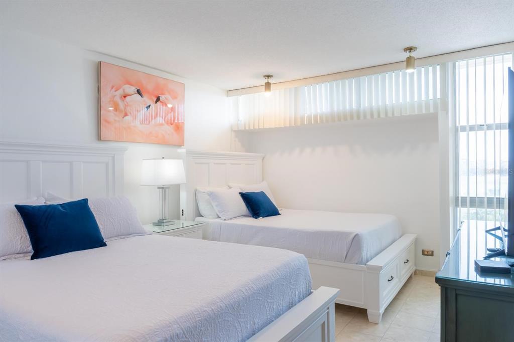 A bedroom features two white beds with blue pillows, a nightstand, and a large painting — 6165 AV, ISLA VERDE UNIT 669, CAROLINA, PR
