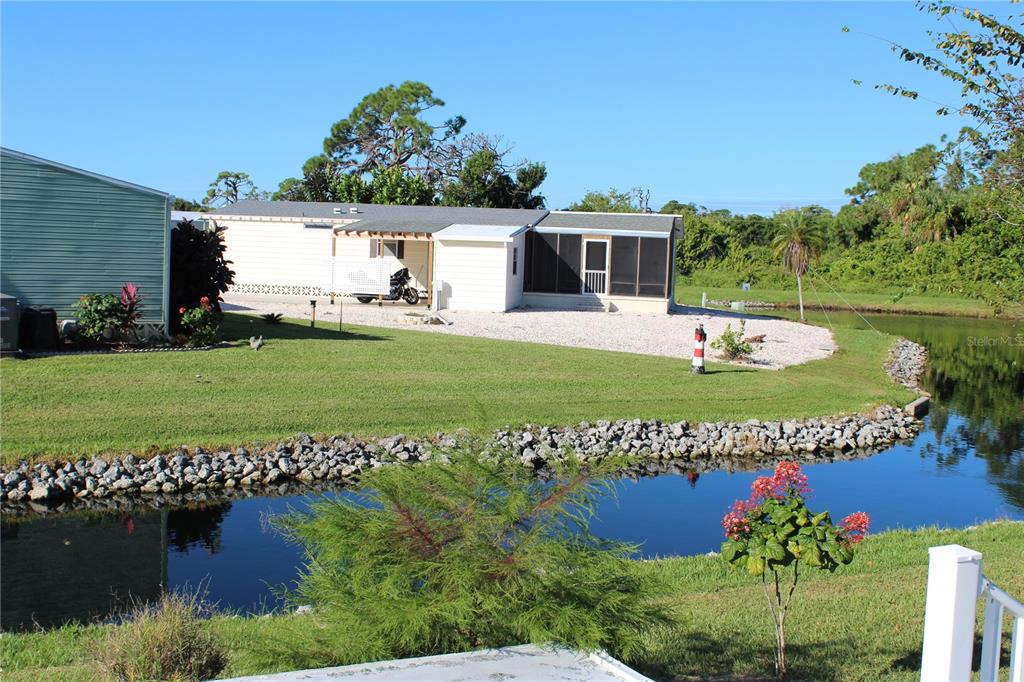 A single-story house with a screened porch sits beside a small canal and lawn — 3304 CATBIRD LANE, ENGLEWOOD, FL