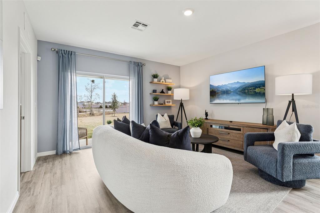 A living room features a curved white sofa, dark armchairs, and a wall-mounted television — 4815 KHLOE COURT, WINTER HAVEN, FL