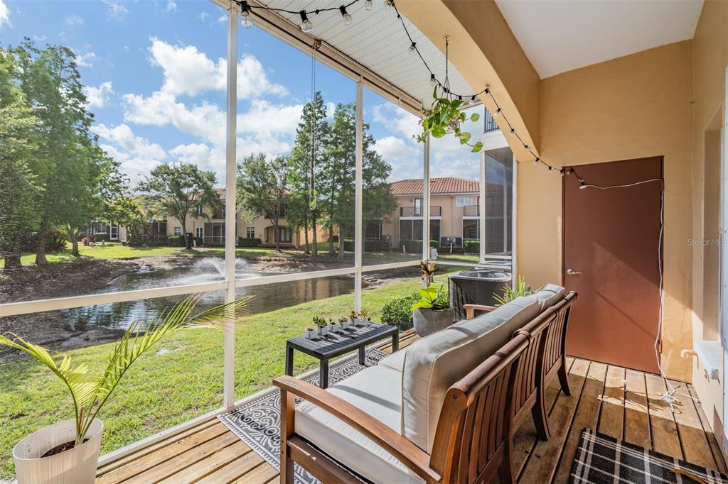 A screened-in porch with a wooden sofa, a small table, and a view of a pond — 415 BARCELONA DRIVE, ST PETERSBURG, FL