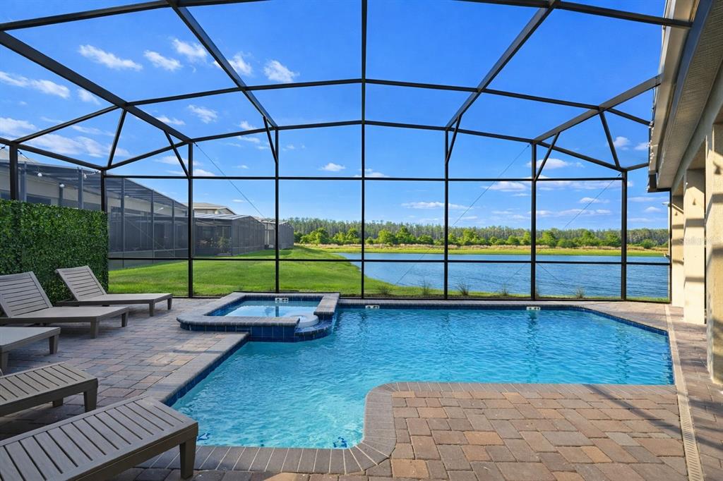 A screened-in pool and spa area overlooks a grassy lawn and a lake — 4221 PARAGRAPH DRIVE, KISSIMMEE, FL