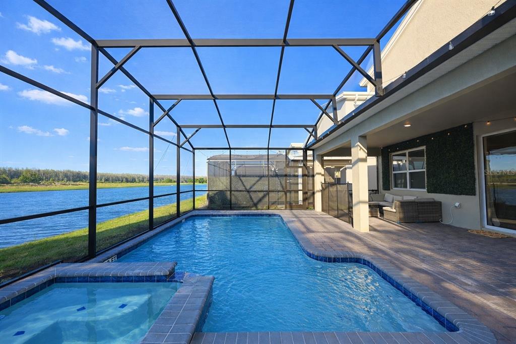 A screened-in pool and spa overlook a lake from a paved patio area — 4221 PARAGRAPH DRIVE, KISSIMMEE, FL