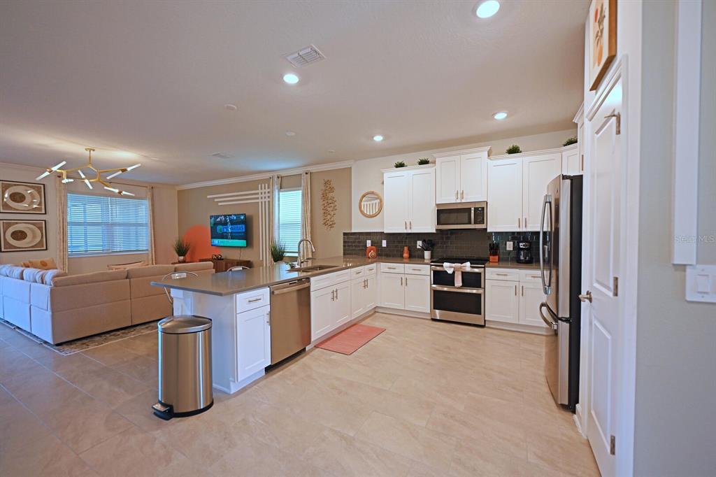 A kitchen with white cabinets and a quartz island opens into a living room area — 4221 PARAGRAPH DRIVE, KISSIMMEE, FL