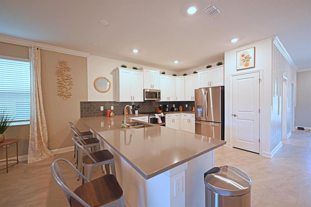 A kitchen features white cabinets, a large quartz island, stainless steel appliances, and tile flooring — 4221 PARAGRAPH DRIVE, KISSIMMEE, FL