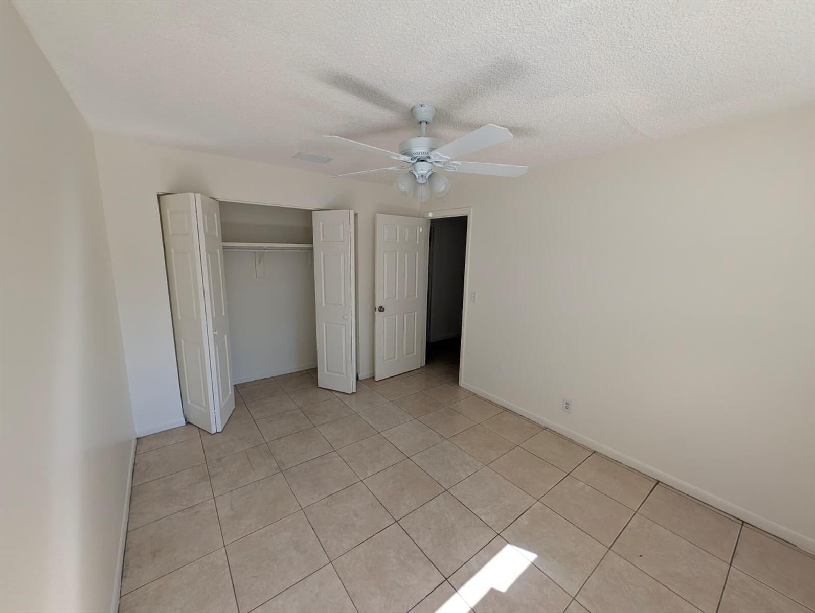An empty bedroom features beige tile flooring, a ceiling fan, and a white closet — 4453 Steven Road # 2, Lake Worth FL 33461, LAKE WORTH, FL