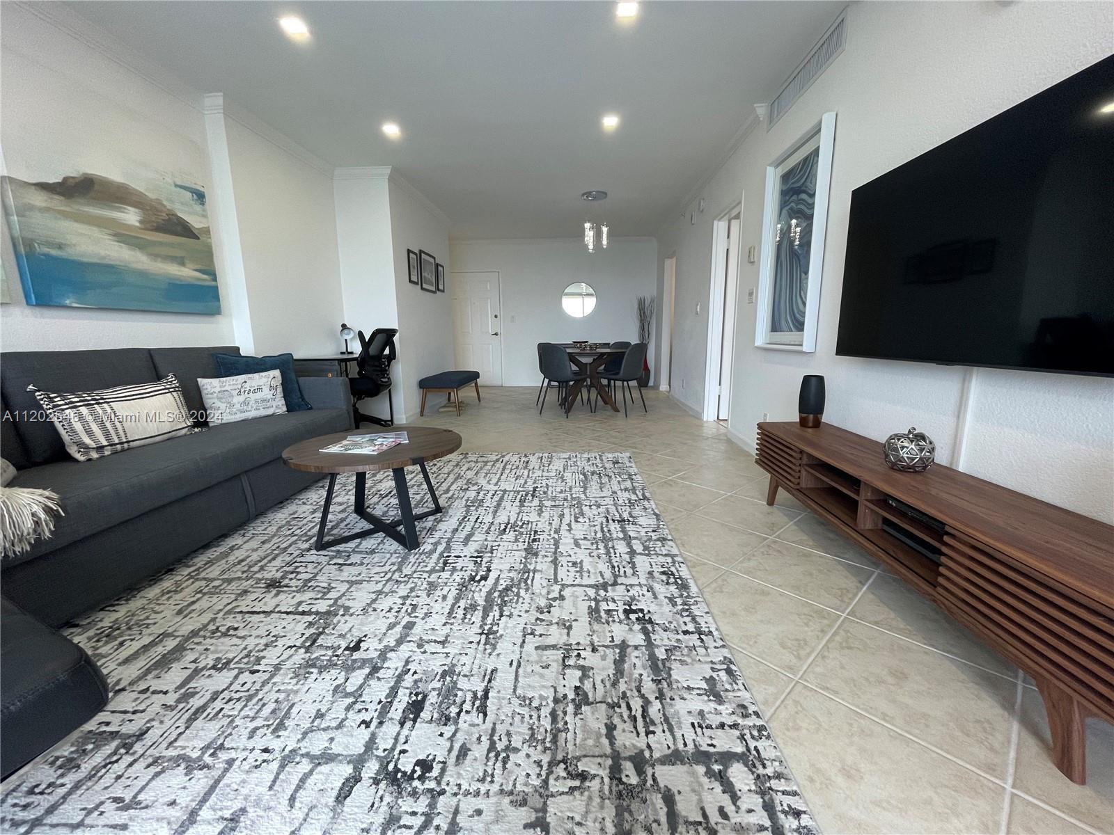 A living room features a gray sofa, a patterned rug, and a wall-mounted television — 2501 S Ocean Dr, Hollywood FL 33019, HOLLYWOOD, FL