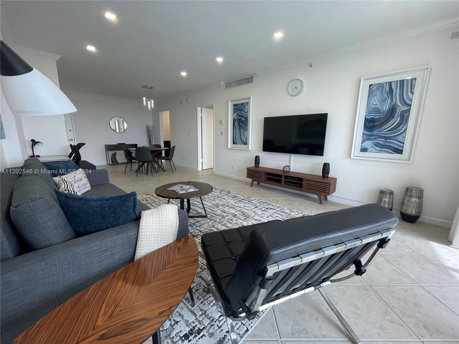 A modern living room features a gray sectional sofa, a black leather chair, and a television — 2501 S Ocean Dr, Hollywood FL 33019, HOLLYWOOD, FL