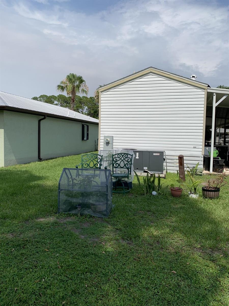 A grassy backyard features a small greenhouse, patio chairs, and an HVAC unit near a house — 3 Mediterranean Boulevard E, Port St. Lucie FL 34952, PORT ST. LUCIE, FL