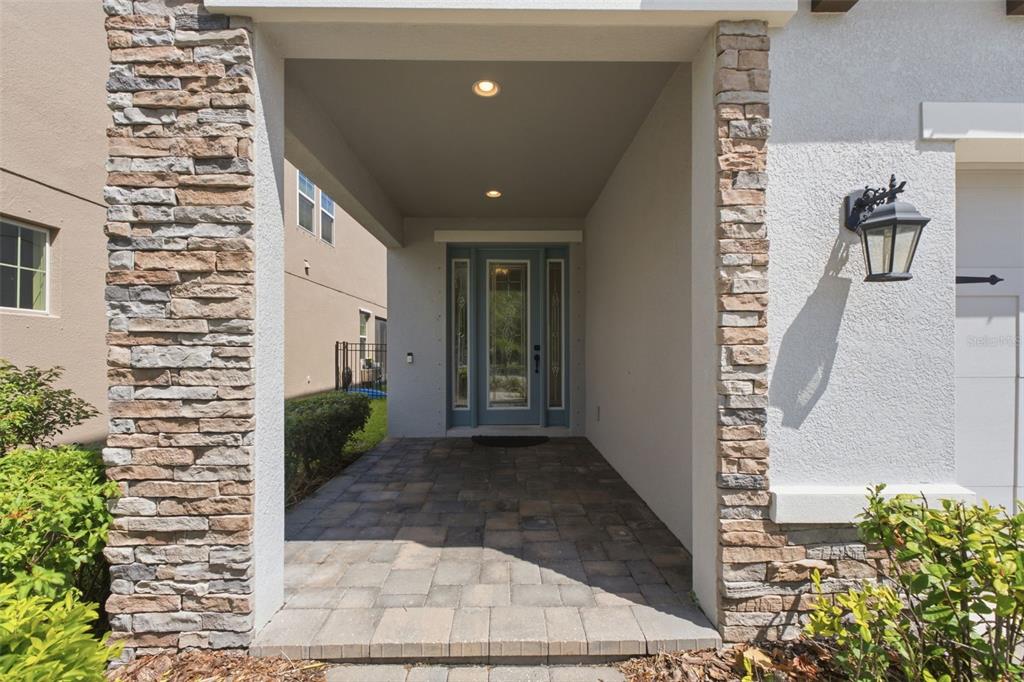 A covered entryway with stone pillars, a paver floor, and a blue front door — 5080 BALLANTRAE BOULEVARD, LAND O LAKES, FL