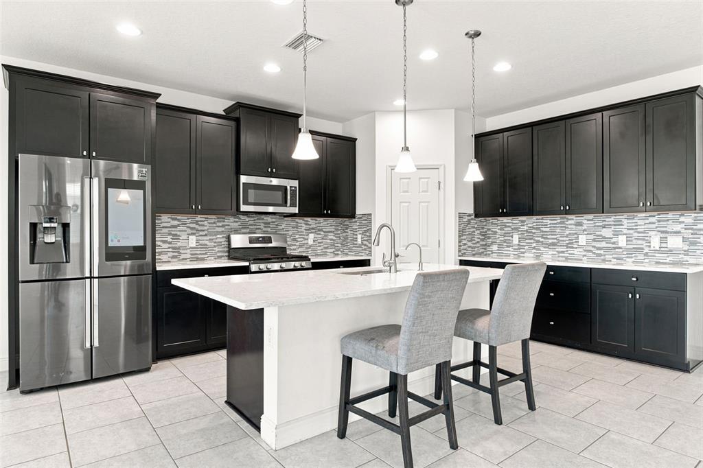 A kitchen features dark cabinets, a white island with two chairs, and stainless steel appliances — 5080 BALLANTRAE BOULEVARD, LAND O LAKES, FL