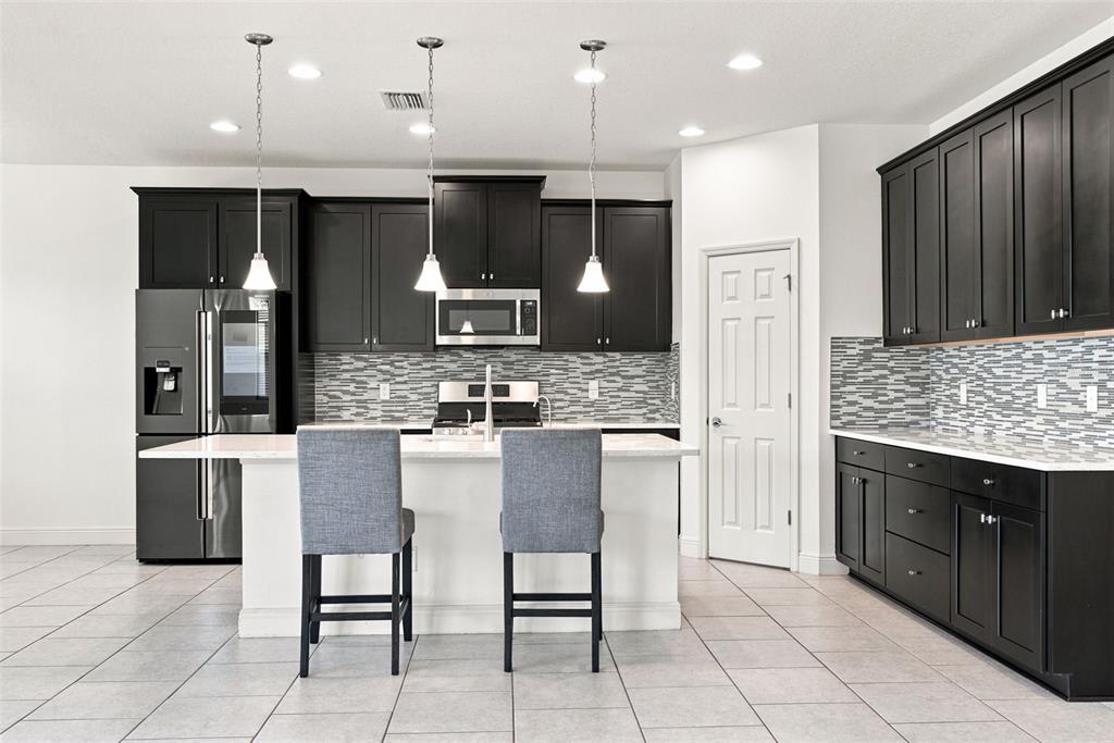 A modern kitchen features dark cabinetry, a white island with two chairs, and tiled flooring — 5080 BALLANTRAE BOULEVARD, LAND O LAKES, FL
