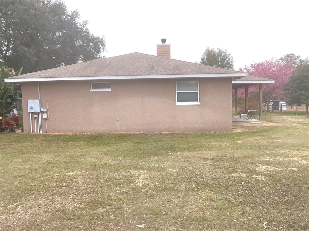 The exterior side of a tan stucco house features a chimney and a covered patio — 32420 COUNTY ROAD 473, LEESBURG, FL