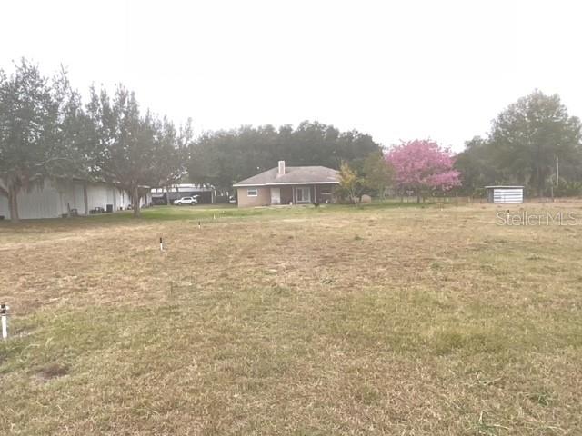 A wide, grassy vacant lot is shown with a house and trees in the background — 32420 COUNTY ROAD 473, LEESBURG, FL