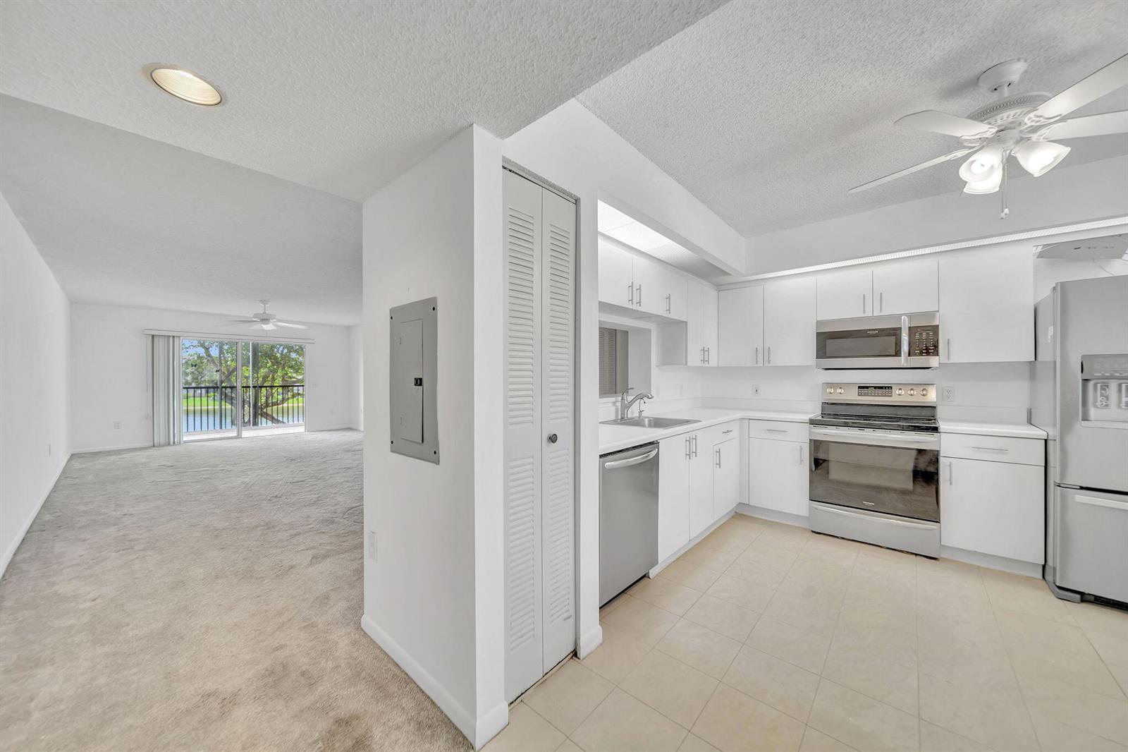 A kitchen with white cabinets and stainless steel appliances opens to a carpeted living area — 801 SW 141st Avenue # o, Pembroke Pines FL 33027, PEMBROKE PINES, FL