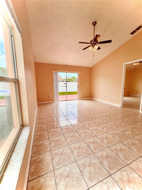 A living room with light-colored tile flooring, a vaulted ceiling, and a sliding glass door — 2416 CONDADO COURT, KISSIMMEE, FL